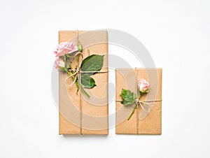 Gift boxes in eco paper on white background. Presents decorated with roses. Holiday concept, top view, flat lay