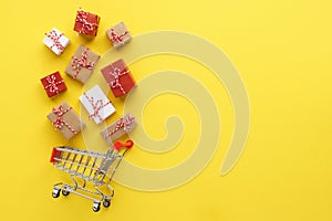 Gift boxes flying out of a shopping cart on yellow background