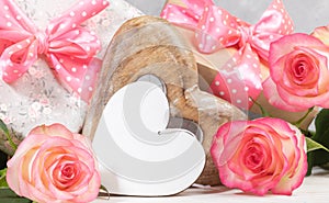 Gift boxes with pink polka dots bows, gentle peach color roses, empty white wooden heart. Close up.