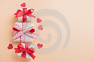 Gift boxes with red ribbon and hearts on pastel beige background.