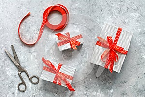 Gift boxes, red silk ribbon and vintage scissors on gray grunge background. Noel. Making handmade gifts. Top view, flat lay