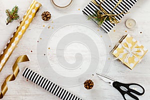 Gift boxes wrapped in black and white striped and goden dotted paper with, pine, cones, candle and wrapping materials on a white w