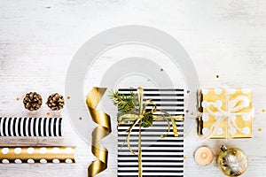 Gift boxes wrapped in black and white striped and golden dotted paper with, pine, cones, candle and wrapping materials on a white