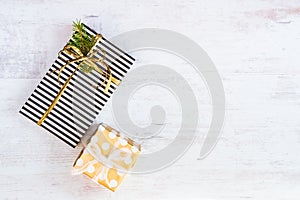 Gift boxes wrapped in black and white striped and golden dotted paper on a white wood background. Christmas presents. Empty space.