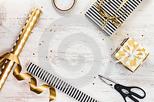 Gift boxes wrapped in black and white striped and golden dotted paper and wrapping materials on a white wood old background. Empty