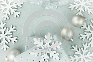 Gift boxes wrapped in silver paper. Curled silver ribbon. Christmas baubles, snow flakes arranged in frame. Copy space for text.