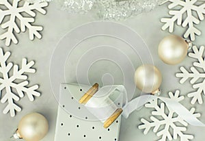 Gift boxes wrapped in silver paper. Wooden spool with white curled silk ribbon, Christmas baubles, snow flakes arranged in frame.