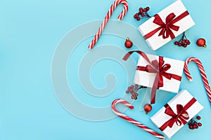 Gift boxes wrapped white paper and red ribbon decorated berries, balls and candy canes on blue background. Top view. Flat lay.