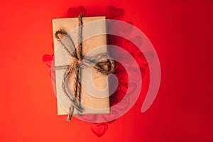 Gift in brown paper on red satin hearts. St. Valentine's Day reb background. Selective focus