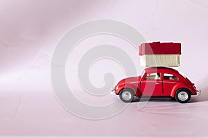 Gift by car. Red toy retro car delivering a gift on a white-pink background. Postcard for New Year, Christmas, Valentine`s Day.