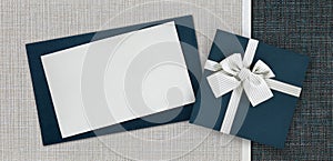 Gift card and gift box with ribbon and bow isolated on elegant blue and grey fabrics background, top view and copy space template