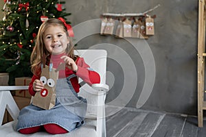 Gift concept for Christmas. Happy little girl with a package of advent calendar sitting at home on an armchair, a