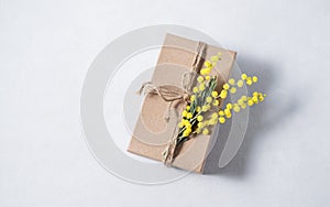 Gift craft box with yellow mimosa flowers on a light background. The concept for the spring holiday of women`s Day or mother`s d