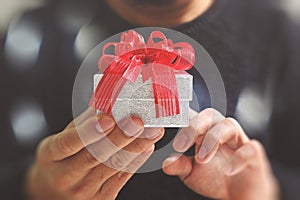 gift giving,man hand holding a gift box in a gesture of giving.blurred background,bokeh effect