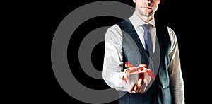 Gift in hand. Happy young business man holding surprise gift box present with red ribbon isolated on black background