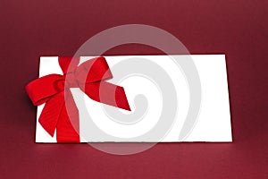 Gift isolated white card with red ribbon bow on deep red background.