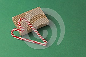 Gift Kraft Brown Color Box and Candy Canes Red and White in Heart Shape Lies on the Green Background, View From the Top. For your