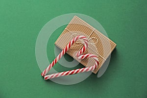 Gift Kraft Brown Color Box and Candy Canes Red and White in Heart Shape Lies on the Green Background, View From the Top. For your