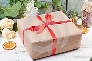 Gift in kraft paper with red satin ribbon on a wooden table flowers