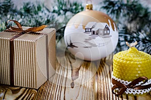 A gift lays on a wooden table next to a candle, cones and an angel against the background of Christmas decorations