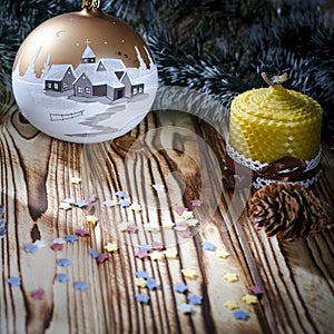 A gift lays on a wooden table next to a candle, cones and an angel against the background of Christmas decorations