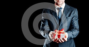 Gift man. Happy young businessman holding surprise gift box present with red ribbon isolated on black background. Black