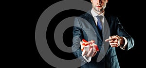 Gift man. Happy young businessman holding surprise gift box present with red ribbon isolated on black background. Black