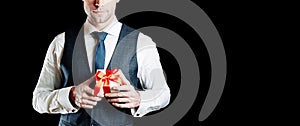 Gift man. Happy young businessman holding surprise gift box present with red ribbon isolated on black background. Black