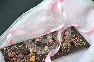 A gift pack of artisan handmade chocolate. Chocolate bars with dried fruit on dark background, front close up view.