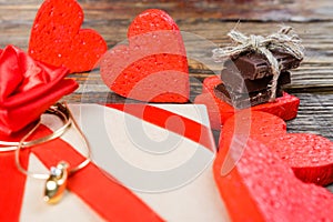 The gift is Packed in Kraft paper and tied with a red ribbon rose. Gift surrounded by decorative heart on one are wedding rings on