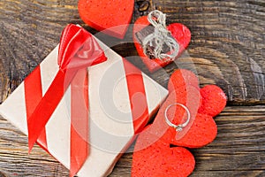 The gift is Packed in Kraft paper and tied with a red ribbon rose. Gift surrounded by decorative hearts one is a wedding ring