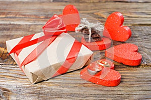 The gift is Packed in Kraft paper and tied with a red ribbon rose. Gift surrounded by decorative heart on one are wedding rings on