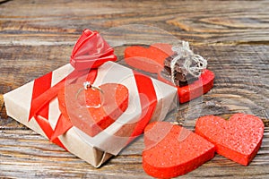 The gift is Packed in Kraft paper and tied with a red ribbon rose. Gift surrounded by decorative heart on one are wedding rings on