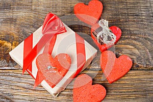 The gift is Packed in Kraft paper and tied with a red ribbon rose. Gift surrounded by decorative hearts one is a wedding ring with