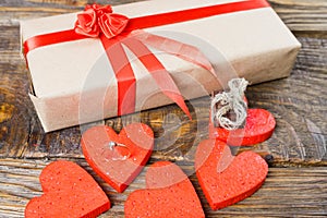 The gift is Packed in Kraft paper and tied with a red ribbon rose. Gift surrounded by decorative hearts one is a wedding ring with