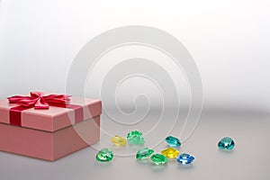 Gift in a pink box on a light background with a copy space. Gift for a girl with gems. Box with a red ribbon