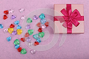 Gift in a pink box on a light background with a copy space. Gift for a girl with gems top view. Box with a red ribbon and coloured