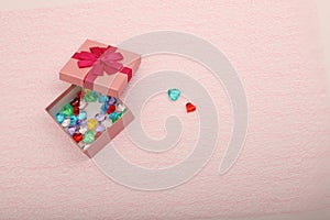 Gift in a pink box on a light background with a copy space. Opened gift box for a girl with coloured hearts inside. Two hearts and