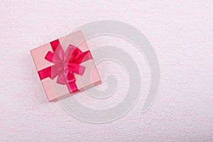 Gift in a pink box on a light pink background with a copy space. Gift box with a red ribbon top view. Simple gift box and copy