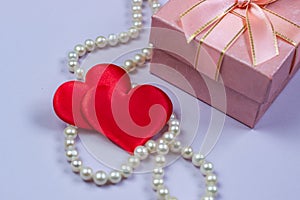 A gift in a pink box with pearls and valentines on a purple background.