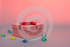 Gift in a pink box on a pink background with a copy space. Gift for a girl with gems. Box with a red ribbon