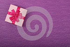 Gift in a pink box on a purple background with a copy space. Gift box with a red ribbon top view