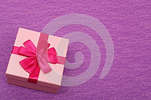 Gift in a pink box on a purple background with a copy space. Gift box with a red ribbon top view