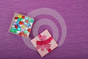 Gift in a pink box on a purple background with copy space. Opened gift box with coloured hearts inside, top view