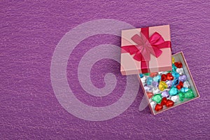 Gift in a pink box on a purple background with copy space. Opened gift box with coloured hearts inside, top view