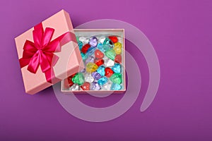 Gift in a pink box on a purple background with copy space. Opened gift box with coloured hearts inside, top view
