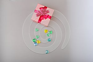 Gift in a pink box with a red ribbon and copy space top view. Gift for a girl with gems. Gift Box with green, yellow and blue gems