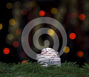 Gift of pink color with a bow on fir branches against a background of yellow and red bokeh lights on a black background