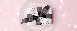 Gift or present box with black satin bow and confetti on pink pastel table top view. Flat lay composition for birthday, mother day