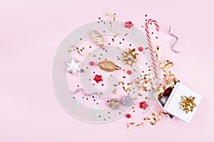 Gift or present box with confetti stars, golden ribbon and holiday decoration on pastel pink background. Christmas flat lay.